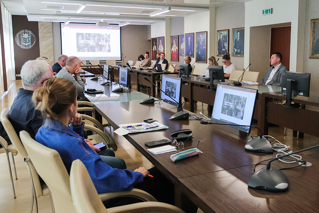 dyrektorzy instytutów przy stole konferencyjnym w sali senackiej słuchają prezentacji przygotowanej przez Wiceprezes Krakowskiego Parku Technologicznego