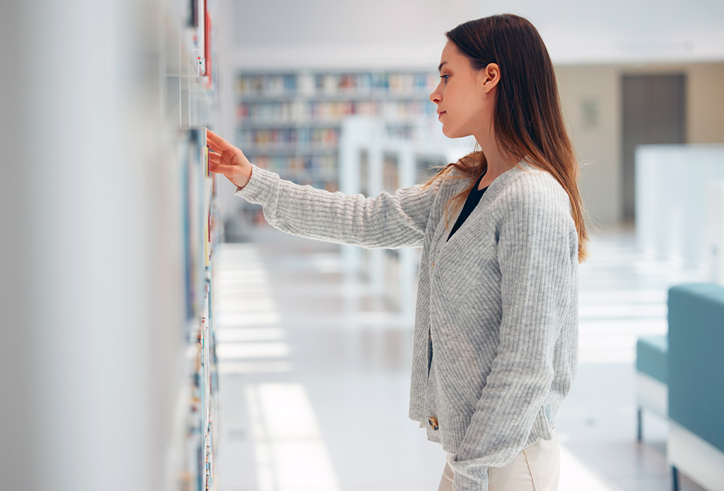 brunetka sięgająca po książkę z bibliotecznej półki