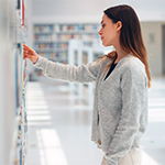 brunetka sięgająca po książkę z bibliotecznej półki