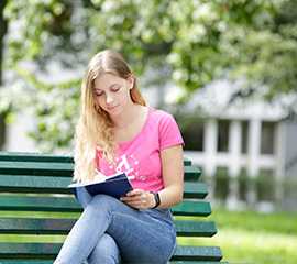 studentka Uniwersytetu Pedagogicznego z książką na ławce przed głównym budynkiem uniwersytetu